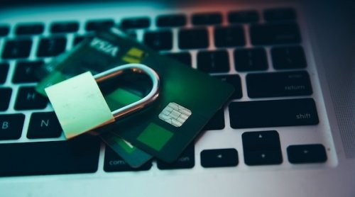 Photographie d'un clavier d'ordinateur, sur lequel sont déposées deux cartes bancaires. Un cadenas fermé est posé sur elles.