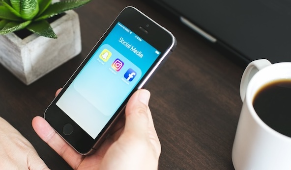 Photographie des mains d'une personne tenant un smartphone, sur lequel s'affichent les icônes de différents réseaux sociaux.