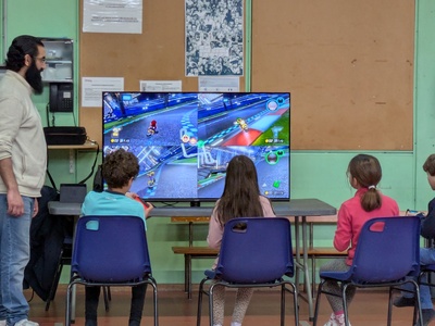 Ce visuel montre trois élèves entrain de faire un tour de piste sur Mario Kart, surveillés par leur enseignant.