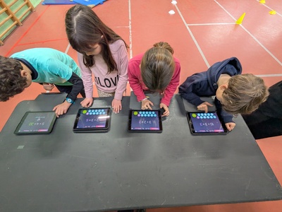 Ce visuel montre 4 élèves entrain de répondre aux questions de calcul mental sur tablette.